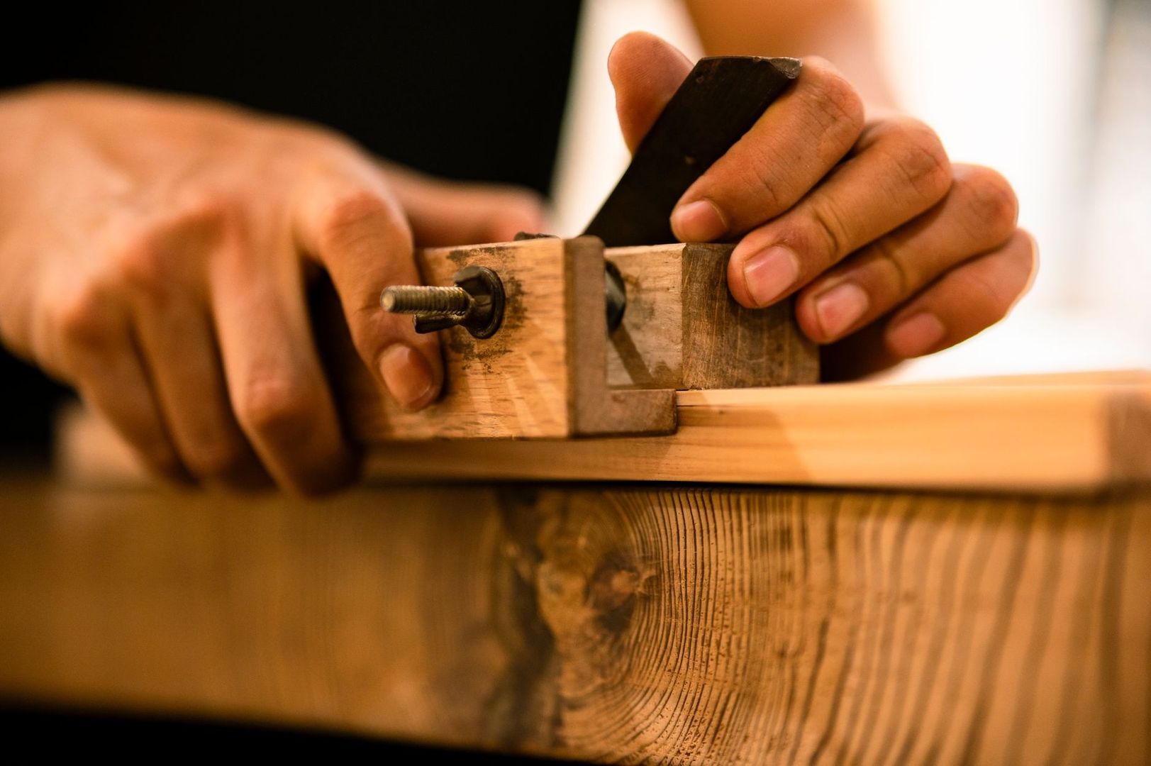 Hände bearbeiten eine traditionelle Holzverbindung mit Hobel und Schraubzwinge